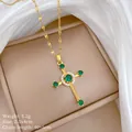Dettaglio del ciondolo a croce dorata con zirconi verdi su sfondo di seta e scatola - Catena In Acciaio Al Titanio Verde A405 Con Pendente Micro-intarsiato In Rame.