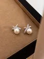 Detailopname van elegante strikvormige pareloorknopjes met glanzende steentjes in een doosje - Kruis Strik Parel Stijl