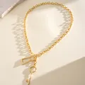 Detailopname van een goudkleurige ketting met unieke hangers in de vorm van een sleutel en slot - Skeletsleutel Ketting / Goud
