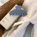 Close-up of a large dusty blue acetate hair claw clip on a minimalist white gift box - Jelly Light Blue