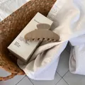 Detail of large khaki acetate hair claw clip placed on white linen fabric inside a basket - Light Chocolate Khaki
