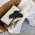 Close-up of a large glossy black acetate claw clip on a white cotton fabric background - Dark Chocolate