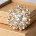 Luxuriöse goldene Blumenbrosche mit funkelnden Kristallen und großem Mittelstein - Goldene Blumige Brosche Mit Weißen Kristallen