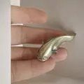 Close-up of a mini antique brass whale figurine held in fingers showing small scale - Catfish