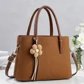 Brown litchi texture tote bag with top handle and floral pendant on marble surface - Brown