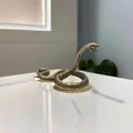 Dettaglio macro di una statuetta di cobra in ottone con scaglie e posa arrotolata - Cobra