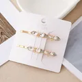 Détail de deux barrettes dorées avec cristaux et nœud papillon sur carte de support - Noeud Avec Zircone Blanche