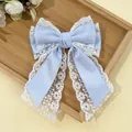 Detailed view of light blue lace bow hair clip with embroidery on a wooden tray - Blue