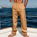 Men's loose khaki linen drawstring trousers for vacation shown in a yacht setting - Earthy Yellow