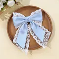 Detail of light blue satin bow hair clip with white lace trim on a wooden tray - Blue