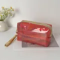 Reddish-pink holographic PVC cosmetic bag with gold zipper and wrist strap for travel. - Red