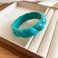 Close-up of a Bohemian turquoise marbled acrylic bangle with twisted texture in a display tray. - Cyan