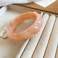 Close-up view of a bohemian peach acrylic bangle featuring unique marble swirl texture. - Pink