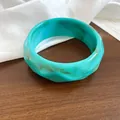 Dettaglio ravvicinato di un ampio bracciale in resina marmorizzata turchese ondulata - Ciano