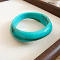 Detailed view of an irregular turquoise acrylic bangle with marbled brown swirls. - Cyan