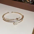 Nahaufnahme eines eleganten zweilagigen Goldarmreifs mit Zirkonia und Kleeblatt-Anhängern - Stil 1 / Gold