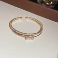 Detailaufnahme des goldenen zweilagigen Armreifs mit Zirkonia-Schleife und funkelnden Steinen. - Stil 3 / Gold