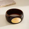 Close-up of chunky dark brown acrylic bangle with marbled oval inset and gold trim - Round Style / Brown And Beige