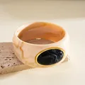 Macro detail of elegant marbled acrylic bangle featuring a large oval black stone with gold trim - Round Style / Ivory And Black