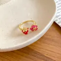 Primo piano dei ciondoli a fragola e fiore in smalto su un anello dorato aperto. - Anello aperto / Stile Rosso-Rosa