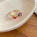 Dettaglio ravvicinato di un anello dorato con fragola rossa e fiore viola in smalto. - Anello aperto / Stile Rosso-Viola