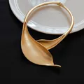 Primo piano di un girocollo in metallo oro opaco con un elegante design a foglia. - Oro Opaco