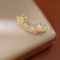 Vista macro detallada de un ear cuff floral bañado en oro 14k con circonitas CZ - Clip (Individual) / Dorado