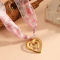Detail shot of a double-heart gold pendant on a delicate pink floral silk scarf necklace. - Hollow Heart Style (K807) / Gold with Pink Scarf