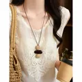 Close-up detail of vintage bohemian woven long necklace worn with white embroidered top - Round Ball Pendant Style (HN12228) / Brown