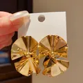 Macro view of gold fan-shaped geometric earrings with high-shine metallic finish - Gold