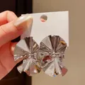 Close-up of retro silver-toned pleated fan-shaped stud earrings on a white display card - Silver