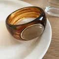 Macro detail of amber acrylic bangle with beige oval stone inlay on a white plate - Coffee-Light Orange