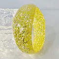 Macro detail of a chunky yellow resin bangle filled with sparkling glitter sequins. - Yellow