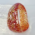 Close-up of a chunky resin bangle filled with colorful glitter and red shards. - Red