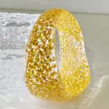 Detailed view of a thick clear resin bangle bracelet with vibrant gold glitter flakes - Orange