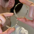 Detail showing gold hoop earrings with sparkling pavé-set zircons held by a person - Bottom Pave Zirconia Design (E2523 Gold) / 925 Silver Needle / Gold
