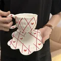 Ceramic coffee cup set with red diamond pattern and heart details in hand-held view - Embossed Red Mesh Cloud Cup 300ml + Saucer 17cm