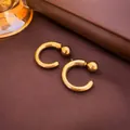 Primo piano dettagliato di orecchini geometrici a forma di C dorati su pelle scura - Oro
