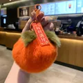 Close-up of a plush orange persimmon keychain featuring a red tag with lucky text. - Persimmon Perfect Score