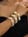 Close-up detail of three chunky stacked irregular gold open cuff bangles on a female wrist - Gold