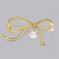 Spilla a fiocco dorata elegante con strass scintillanti e una perla bianca pendente. - Perla Pendente Fiocco