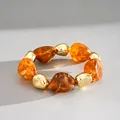 Detailopname van een retro armband met onregelmatige amberkleurige acrylkralen en goud - Geometrische Patchwork Armband / koffiekleur