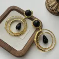 Close-up of golden textured metal earrings with black resin teardrops on a wooden stand - Gold-Black