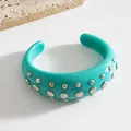 Dettaglio di un bracciale a polsino in resina turchese con borchie in metallo - Bangle / Ciano