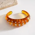 Dettaglio raffinato di un elegante bracciale rigido in resina ambrata con borchie. - Bangle / Marrone