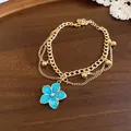 Detail view of a layered gold bracelet with a vibrant blue enamel flower pendant. - Bracelet / Blue