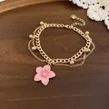 Detailed macro shot of golden multi-layer bracelet featuring a pink enamel flower pendant - Bracelet / Pink