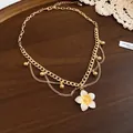 Close-up detail of a golden necklace featuring a sweet white flower pendant for summer - Necklace / White