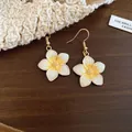 Close-up detail of yellow and white enamel flower drop earrings on a wooden background - Earring Hooks / White