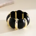 Gros plan d'un bracelet en acrylique noir et doré avec une finition mate élégante. - Bracelet - Blocs Circulaires / Or-Noir